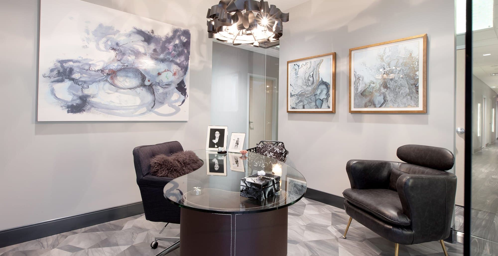 A consultation lounge at Acqua Blu Medical Spa, with a sculptural chandelier, original artwork, and a glass table