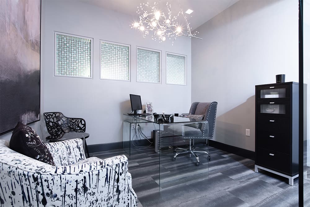 A consultation office with a glass desk beneath a chandelier